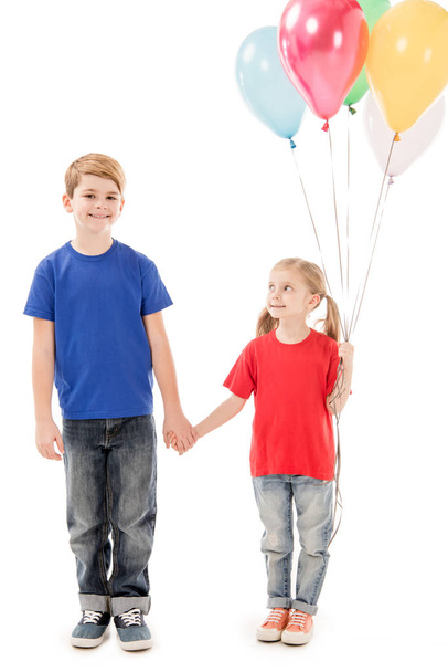 full length view of two kids with colorful balloons holding hands isolated on white - 写真・画像