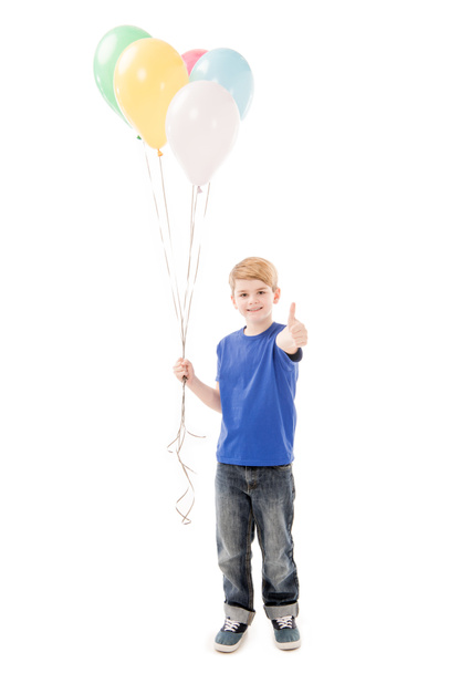 full length view of smiling kid holding colorful balloons and showing thumb up isolated on white - Fotoğraf, Görsel