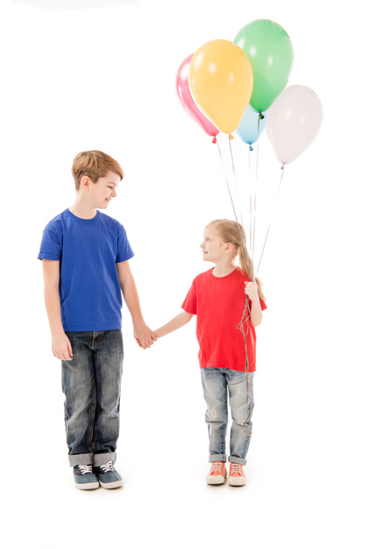 full length view of two kids with colorful balloons holding hands isolated on white - Valokuva, kuva