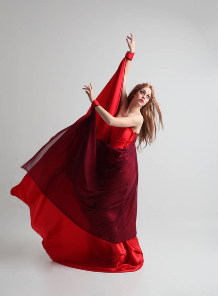 full length portrait of a  girl wearing a long red silk gown, Standing pose on a grey studio background. - Fotó, kép