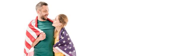 Panoramaaufnahme eines lächelnden Paares mit amerikanischer Flagge, das einander umarmt und isoliert auf Weiß betrachtet - Foto, Bild