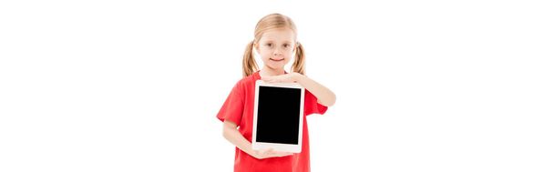 Panoramaaufnahme eines lächelnden Kindes in rotem T-Shirt, das ein digitales Tablet mit leerem Bildschirm hält, isoliert auf weiß - Foto, Bild