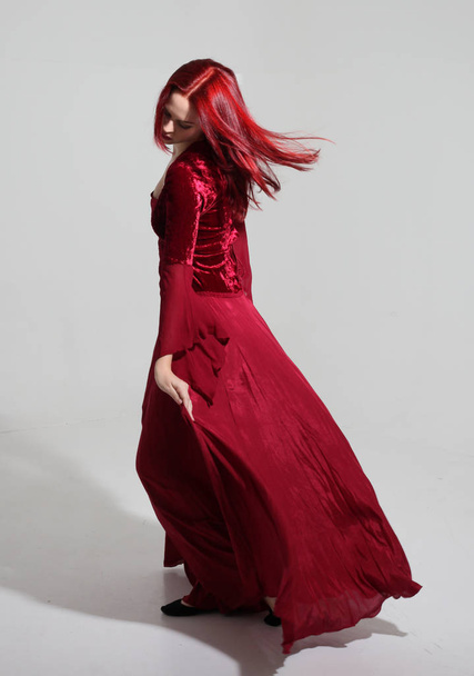 full length portrait of a  girl wearing a  red medieval fantasy gown, Standing pose on a grey studio background. - Photo, Image