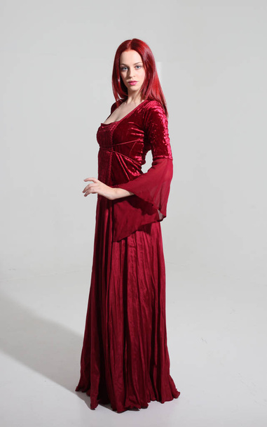 赤い中世のファンタジーガウンを着た女の子の完全な長さの肖像画、灰色のスタジオの背景に立っているポーズ. - 写真・画像