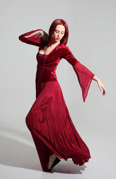 ολόσωμο πορτρέτο ενός κοριτσιού που φοράει ένα κόκκινο μεσαιωνικό φόρεμα φαντασίας, στέκεται ποζάρει σε ένα γκρίζο φόντο στούντιο. - Φωτογραφία, εικόνα