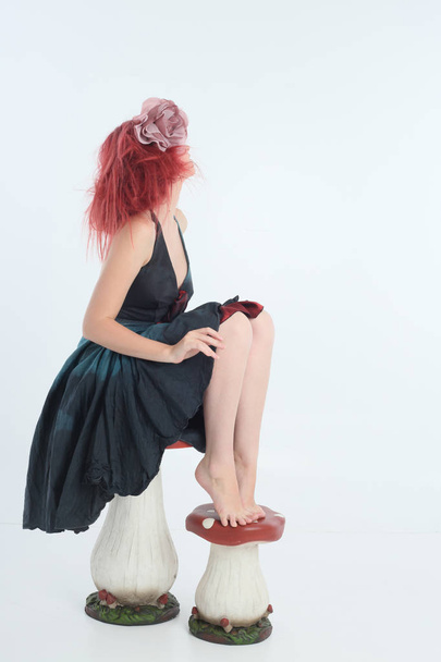 портрет рудої волохатої дівчини в костюмі феї, позу сидячи на білому студійному фоні з грибними реквізитами
. - Фото, зображення