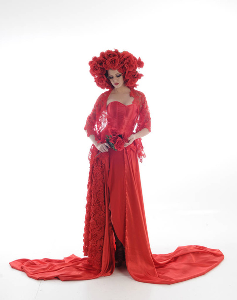 portrait pleine longueur de fille portant longue robe de soie rouge et coiffe de fleurs. pose debout sur fond de studio blanc. - Photo, image