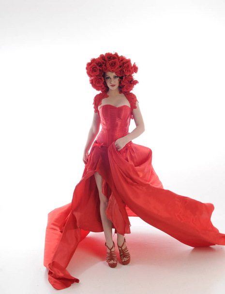 volledig portret van het meisje met lange rode zijden jurk en bloemenhoofdtooi. staande houding op witte studio achtergrond. - Foto, afbeelding