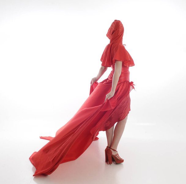 ολόσωμο πορτρέτο της γυναίκας που φοράει κόκκινη κάπα γάντζο και μακρύ μεταξωτό φόρεμα. όρθια πόζα, απομονωμένη σε λευκό στούντιο φόντο - Φωτογραφία, εικόνα