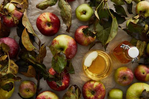 Top zicht op rijpe appels met bladeren in de buurt van glas en fles cider - Foto, afbeelding