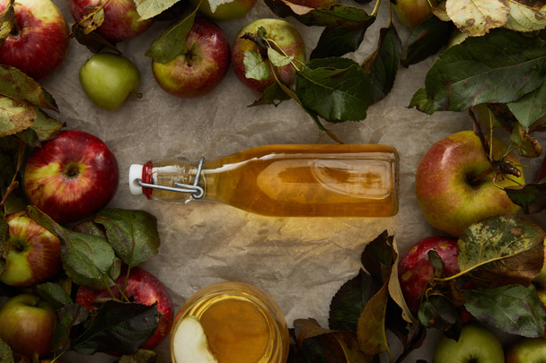 bovenaanzicht van fles met cider tussen appels en glas met drank op Perkamentpapier met Kopieer ruimte - Foto, afbeelding