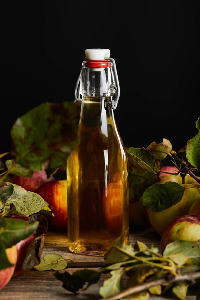 fresh homemade cider in bottle near ripe apples and leaves on wooden surface isolated on black - Foto, Bild