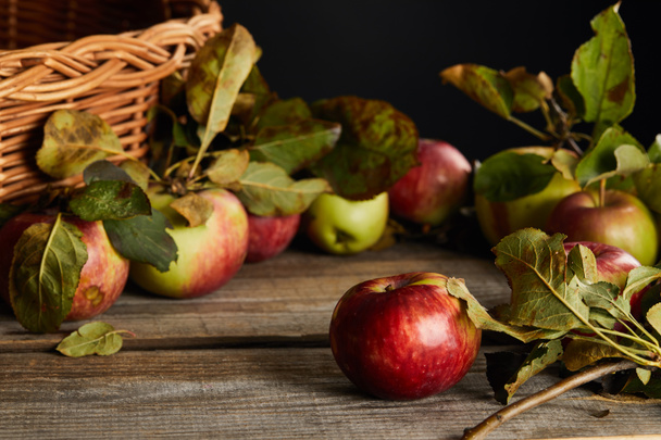 wooden surface with apples and leaves near wicker basket isolated on black - Foto, Imagen