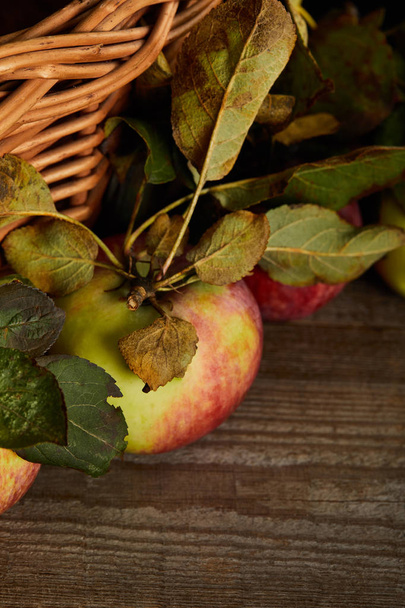 vista de cerca de manzanas maduras cerca de la canasta de mimbre en la superficie de madera marrón
 - Foto, Imagen