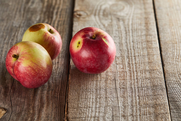 яблоки с небольшим гнилым пятном на деревянной поверхности
 - Фото, изображение