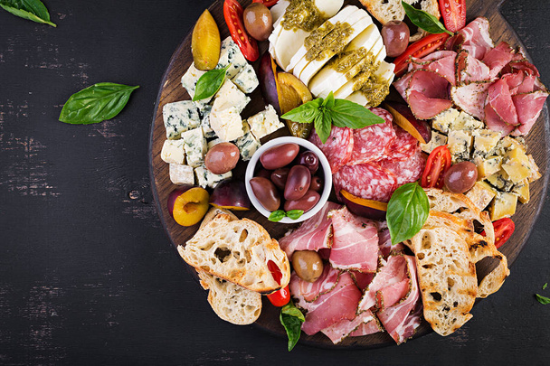 Antipasto schotel met ham, prosciutto, salami, blauwe kaas, mozzarella met pesto en olijven op een houten achtergrond. Bovenaanzicht, overhead - Foto, afbeelding