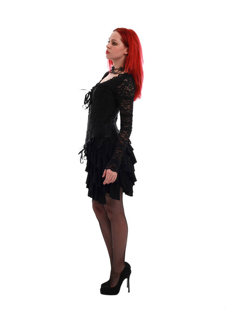 full length portrait of a  red haired girl wearing a  black gothic gown, Standing pose on a grey studio background. - Foto, Bild