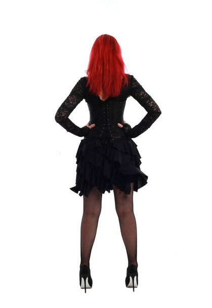 full length portrait of a  red haired girl wearing a  black gothic gown, Standing pose on a grey studio background. - Fotografie, Obrázek