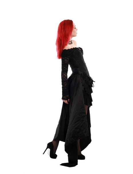 full length portrait of a  red haired girl wearing a  black gothic gown, Standing pose on a grey studio background. - Foto, Imagem