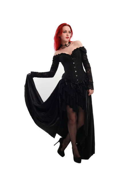 full length portrait of a  red haired girl wearing a  black gothic gown, Standing pose on a grey studio background. - Foto, immagini