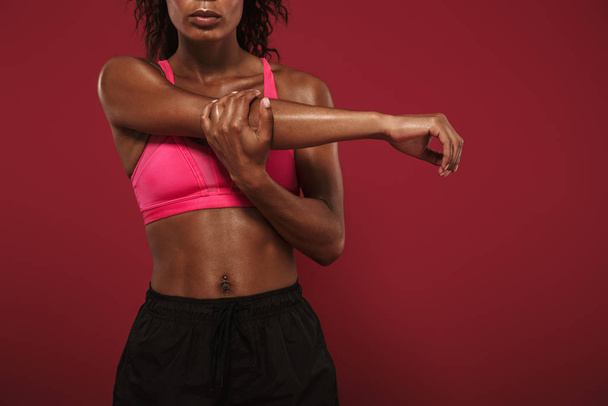 Concentrated strong young african fitness sports woman posing isolated over red wall background make stretching exercises. - Photo, Image