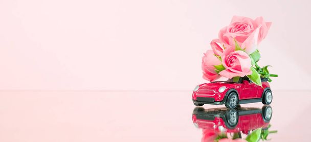 Red toy car delivering bouquet of pink rose flowers on pink background. Banner. Place for text. Mirror reflection. February 14 card, Valentine's day. Flower delivery. 8 March, Happy Women's Day. - Foto, Bild