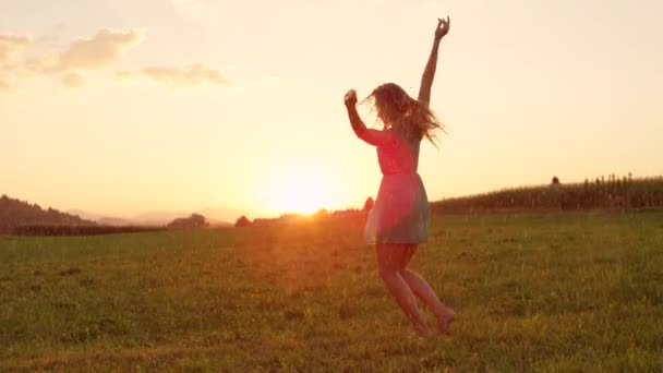 LENT MOTION, LENS FLARE : Une jeune femme caucasienne détendue danse librement dans une belle prairie au lever du soleil. Jolie fille aux cheveux blonds filant sous la pluie lors d'une soirée tranquille dans la campagne idyllique
. - Séquence, vidéo