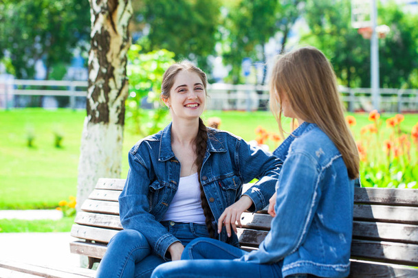 Two beautiful girlfriends are talking in a park sitting on a ben - Foto, Imagen