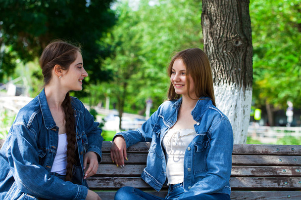 二人の美しいガールフレンドがベンの上に座っている公園で話しています - 写真・画像