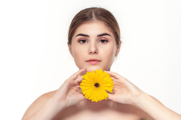 Крупным планом портрет красивой молодой девушки с желтым цветком на белом фоне
. - Фото, изображение