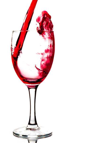 κόκκινο κρασί είναι χύνεται ένα ποτήρι κρασί που απομονώνονται σε λευκό φόντο - Φωτογραφία, εικόνα