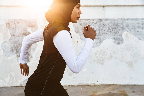 Strong muslim sports fitness woman dressed in hijab and dark clothes running outdoors. - Fotografie, Obrázek