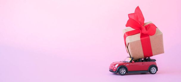 Banner with red toy car delivering gift box with red ribbon on pink background. Place for text. Sales, Birthday, christmas time - Foto, immagini