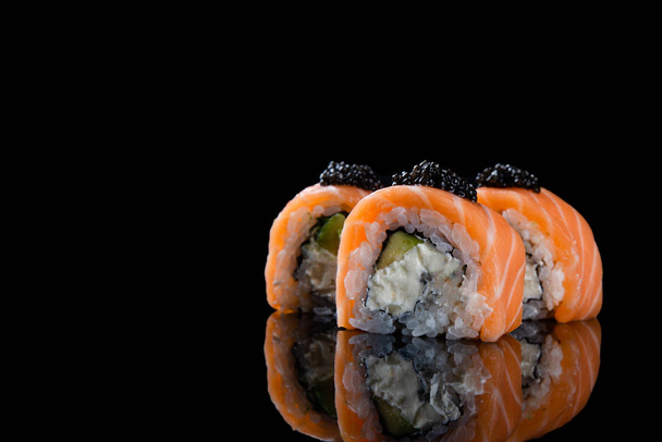 Σούσι roll Φιλαδέλφεια με σολομό, καπνιστό χέλι, αβοκάντο, τυρί κρέμα σε μαύρο φόντο. Ιαπωνικό φαγητό. - Φωτογραφία, εικόνα