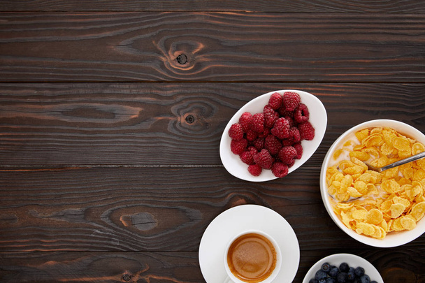 kahve fincan ı ve ahşap yüzeyüzerinde taze çilek tabakları yakınında mısır gevreği ile kase üst görünümü - Fotoğraf, Görsel