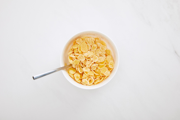 top view of bowl of cornflakes with spoon on white marble surface - Foto, immagini