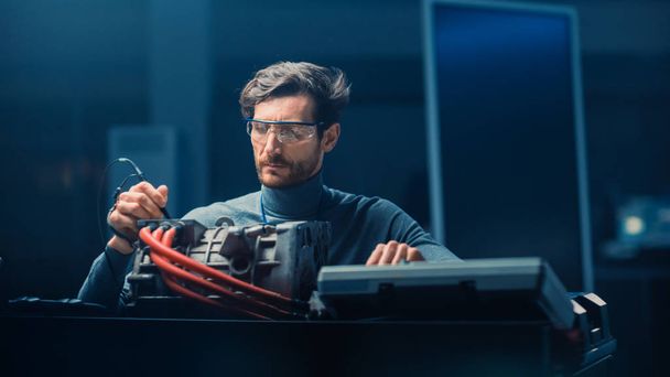 Professional Automotive Engineer in Glasses with a Computer and Inspection Tools is Testing an Used Electric Engine in a High Tech Laboratory with a Concept Car Chassis. - Photo, image