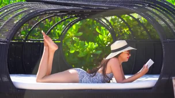 footage of beautiful Asian woman reading book in sunbed outdoors - Felvétel, videó