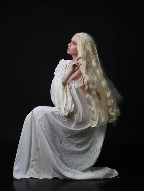 Beyaz bir cüppe giyen uzun sarı saçlı bir kadının hayalet portresi. siyah bir stüdyo arka plan karşı poz.  - Fotoğraf, Görsel