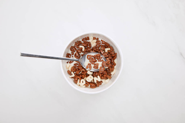 top view of bowl with chocolate and white cereal with milk and spoon on marble surface - Photo, Image