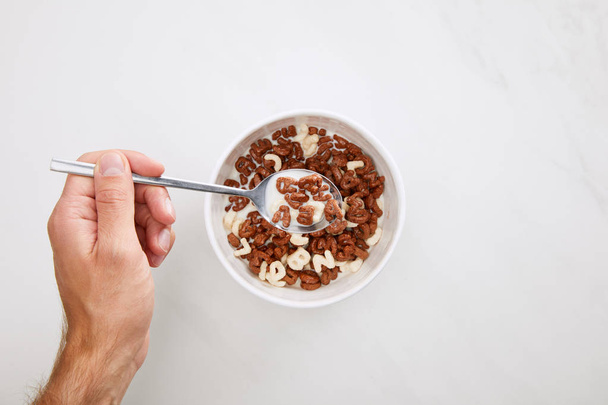 cropped image of man taking cereal with spoon from bowl on marble surface - Foto, Imagem