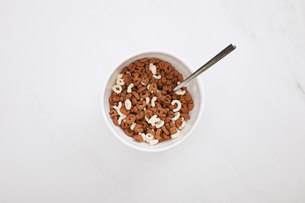 top view of bowl with chocolate and white cereal and spoon on marble surface - Photo, Image