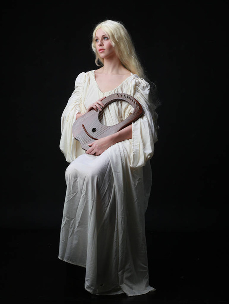Beyaz bir cüppe giyen uzun sarı saçlı bir kadının hayalet portresi. siyah bir stüdyo arka plan karşı poz.  - Fotoğraf, Görsel