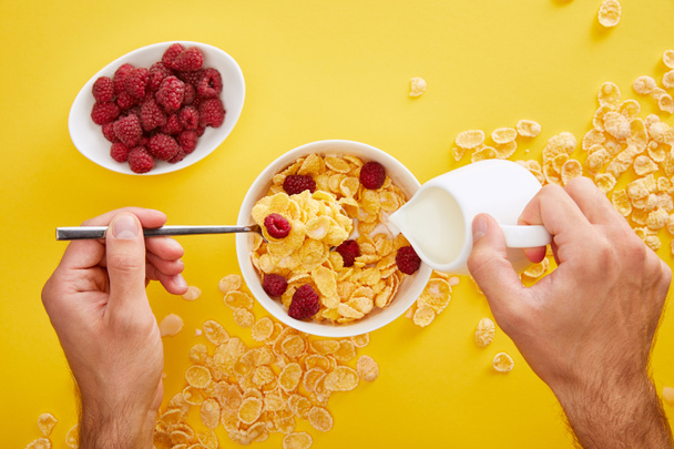 cropped view of man pouring milk into bowl with cornflakes isolated on yellow - Photo, Image