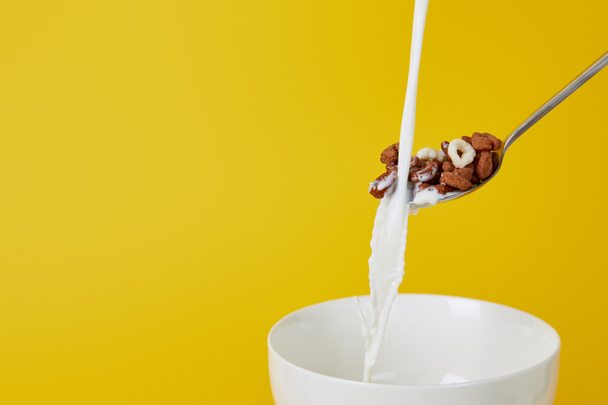 spoon with assorted cereal and milk stream above white bowl isolated on yellow - Photo, Image