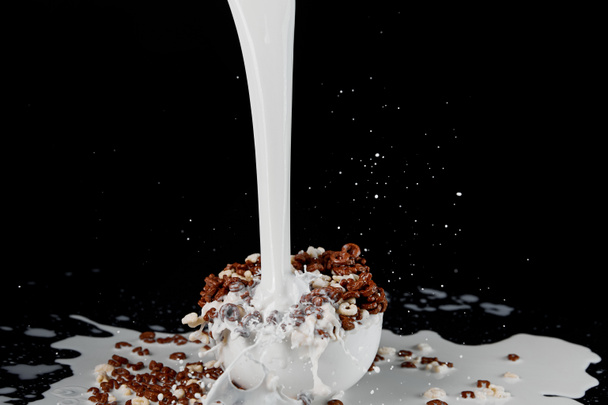Biała miska z wyborem płatków zbożowych z silnym strumieniem mleka na czarno - Zdjęcie, obraz