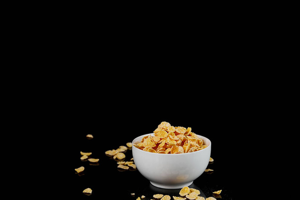 white bowl with cornflakes and scattered pieces isolated on black - Photo, Image