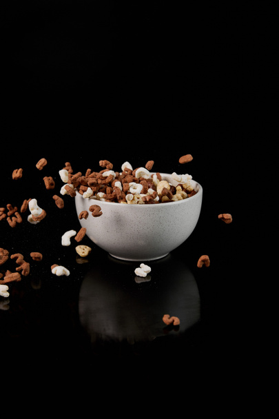 white bowl with cereal and dropped pieces isolated on black - Fotó, kép