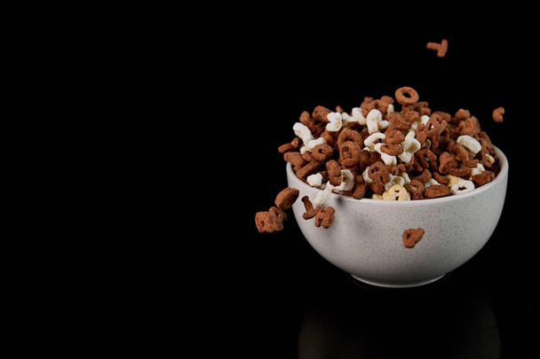 tigela branca com cereais e pedaços dispersos isolados em preto
 - Foto, Imagem