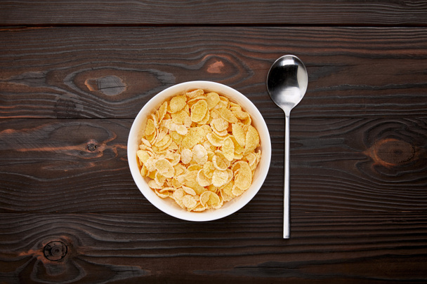 top view of spoon near cornflakes in bowl on wooden surface - Foto, Imagem